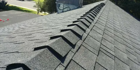 Close-up of a gray asphalt shingle roof with a row of ridge vent channels along the peak.